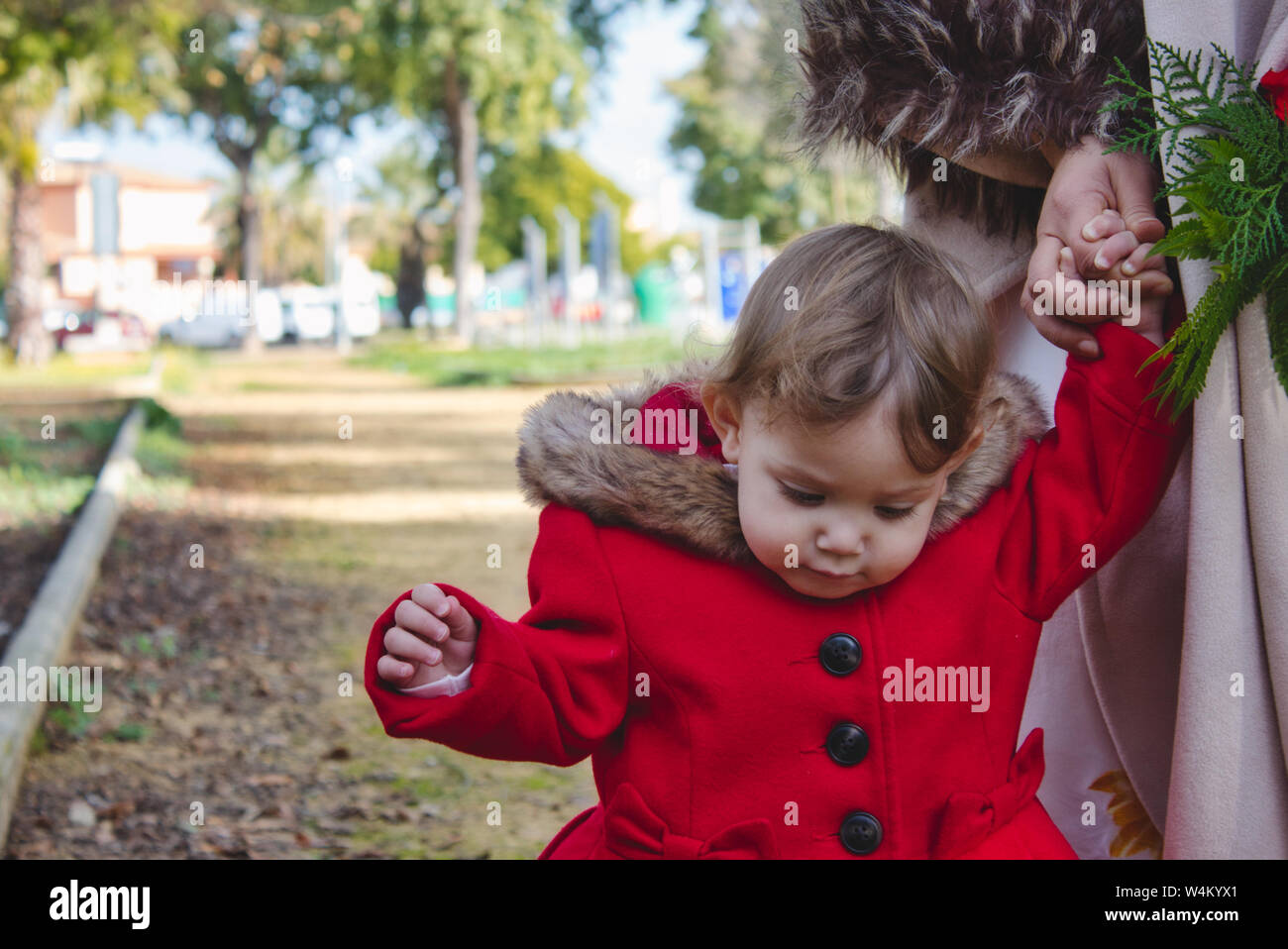 Petite fille qui marche main dans la main avec sa mère sur un chemin à l'extérieur dans un parc en hiver Banque D'Images