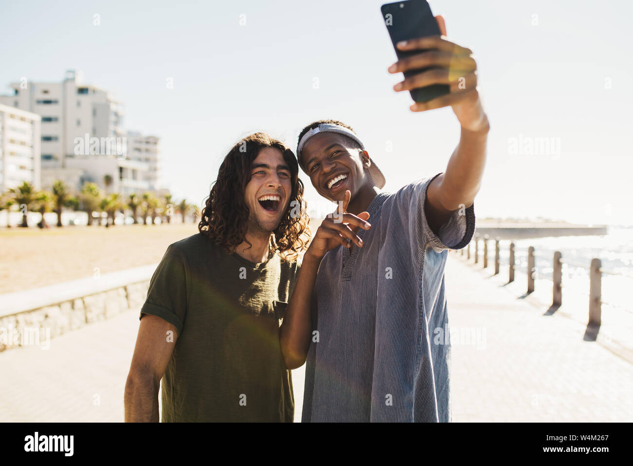 Deux jeunes hommes de race mixte faisant une promenade en bord de mer. par selfies Happy young friends taking self portrait avec un téléphone intelligent à l'extérieur. Banque D'Images