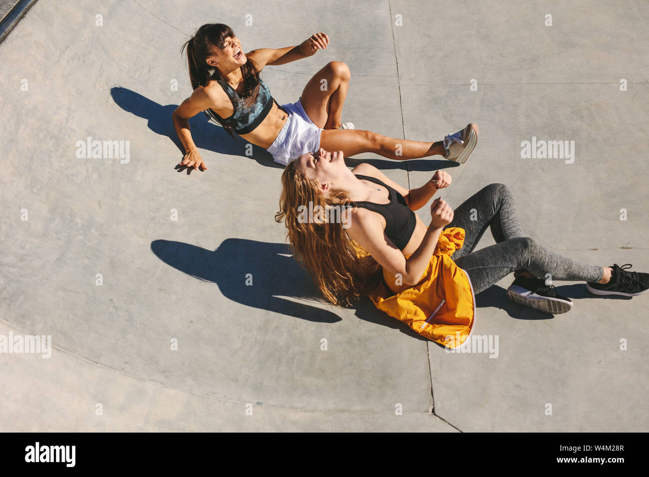 Les filles assis à skate bowl et rire. Les femmes les amis de détente en plein air au skate park. Banque D'Images