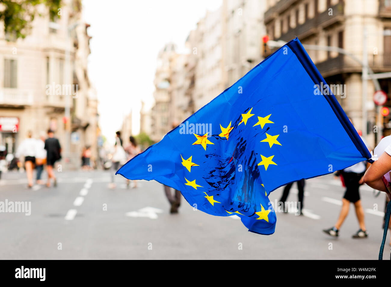 Jeune personne marche dans les rues en plein jour holding drapeau de l'Union européenne avec des taches de sang sur elle pour protester contre les politiques d'immigration Banque D'Images