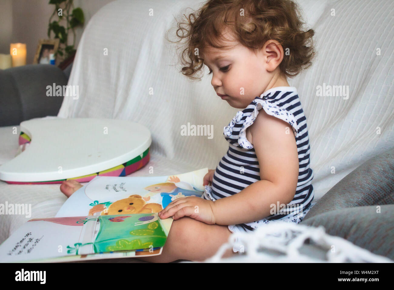 Petite fille lisant un livre d'images sur un canapé blanc Banque D'Images