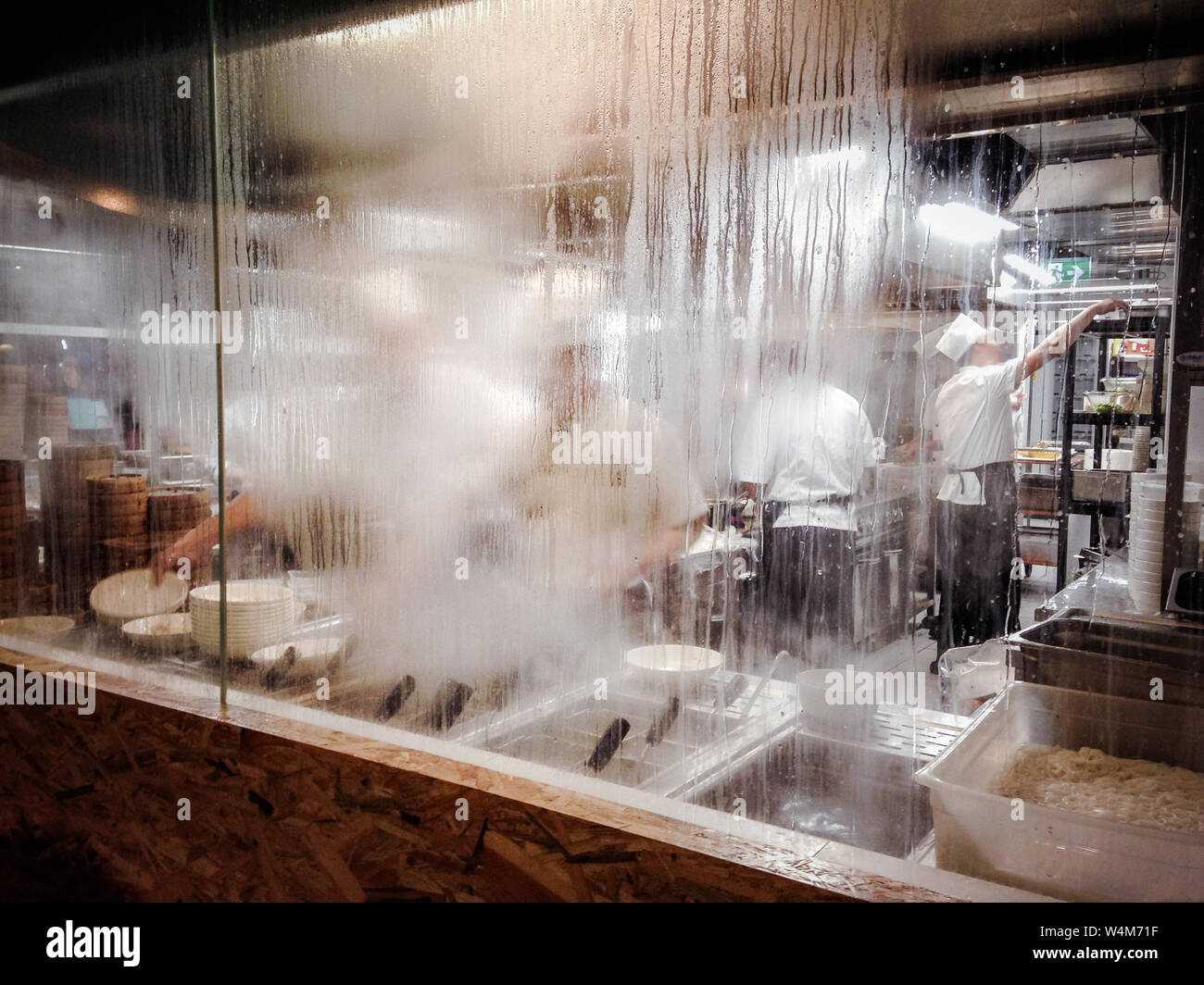 Vue d'une cuisine de restaurant avec plusieurs cuisiniers au travail. Il y a beaucoup de vapeur et de condensation Banque D'Images