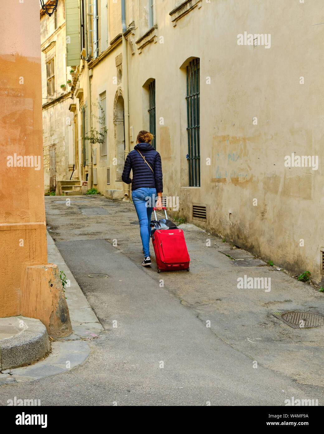 Jeune femme, marche à pied, tirant une valise roulant rouge en bas de la rue étroite de la vieille ville à Arles, France Banque D'Images