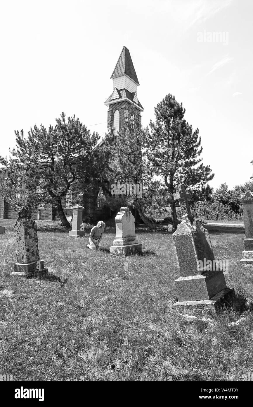 Pays abandonner Grave yard avec ancienne église avec de vieux et tumestones femme priant et en rendant hommage à ses secouristes à sur ses genoux dans le culte. Banque D'Images