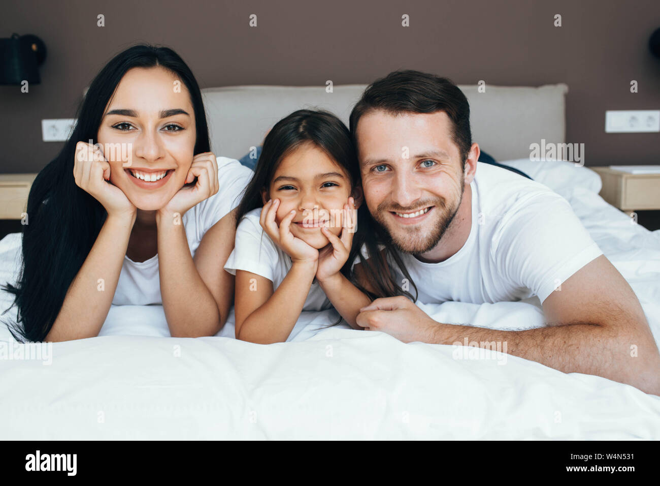 Famille heureuse sur un lit, regardant la caméra. Mère, père et fille lying on bed at home Banque D'Images