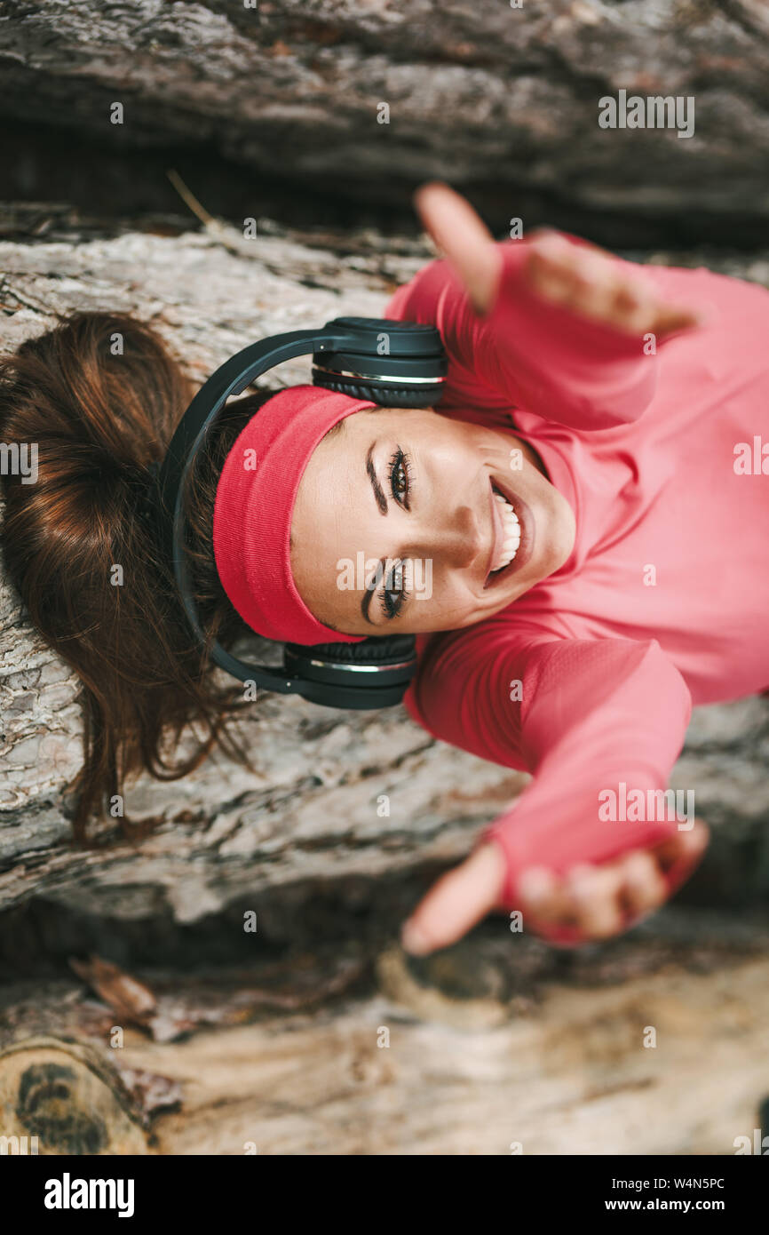 Young female runner couché sur un journal en bois et faire une pause avec la musique après une marche en forêt. Elle est donne à ses mains comme s'appeler quelqu'un à Banque D'Images