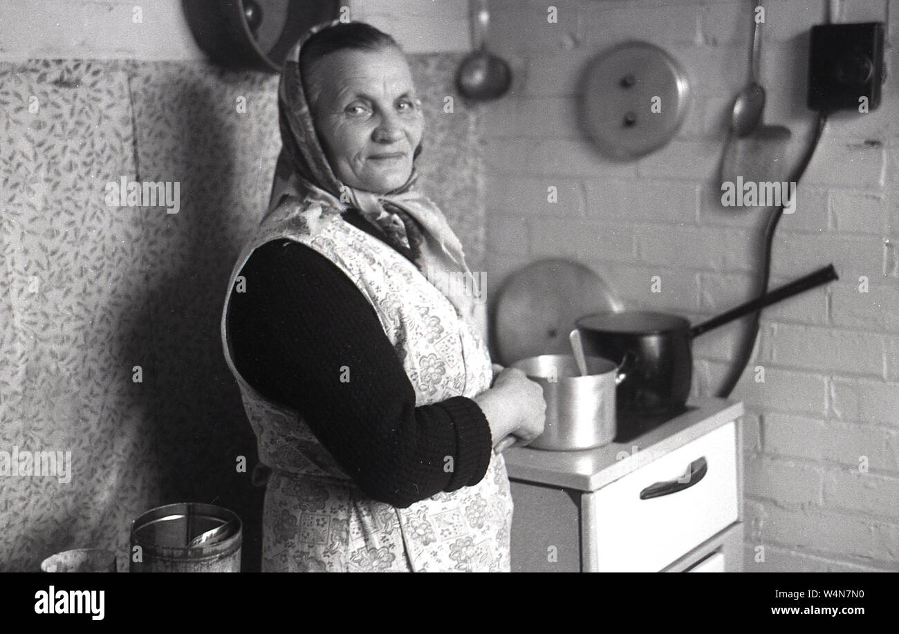 Années 1950, historiques, une femme dans une petite cuisine, le port d'un foulard et pinafore, un cuisinier pour une petite pépinière. Banque D'Images