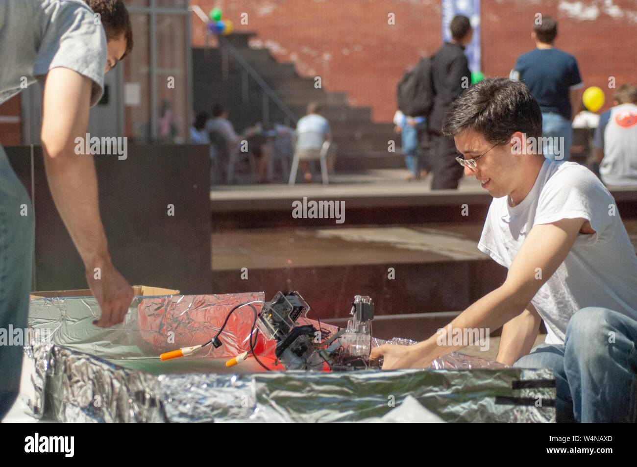 Deux personnes, à l'extérieur par une journée ensoleillée, le cintrage de la sorte à travers un enchevêtrement de l'équipement électrique dans une boîte doublée de papier d'aluminium, en préparation d'une partie du Centre des Arts Mattin à la Johns Hopkins University, Baltimore, Maryland, le 4 mai 2007. À partir de la collection photographique de Homewood. () Banque D'Images