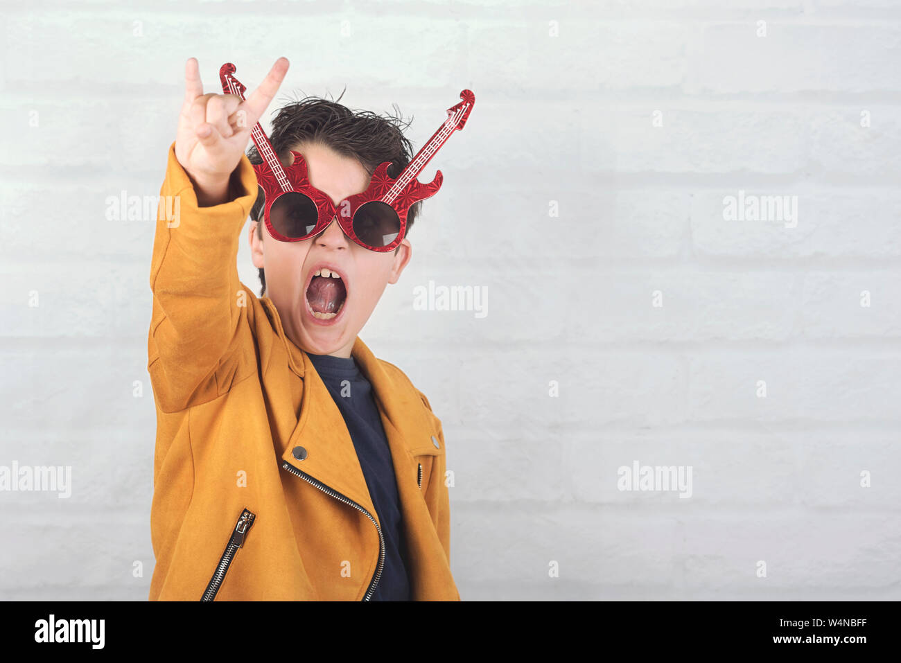 Enfant avec des lunettes faisant symbole rock avec les mains à fond brique Banque D'Images