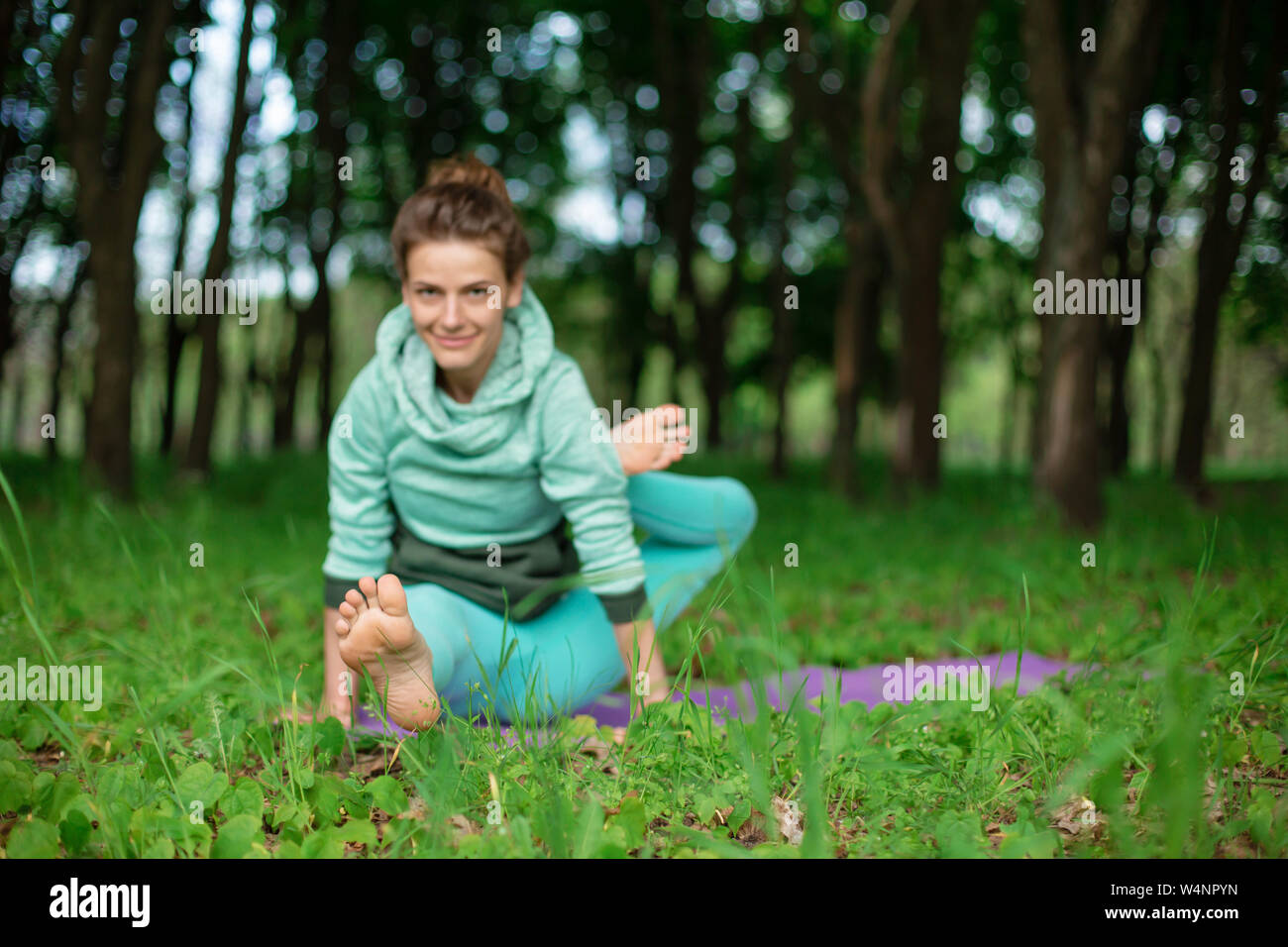 Brunette mince fille joue et exécute des sports belle et sophistiquée postures de yoga dans un parc d'été. Luxuriante forêt verte sur l'arrière-plan. Femme Banque D'Images