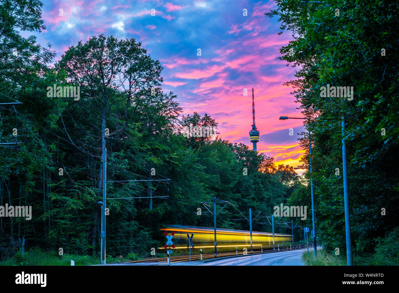 Allemagne, Stuttgart city tour de télévision en vert forêt avec ciel rougeoyant après le coucher du soleil à partir de la rue avec trafic tramway dans la belle nature paysage Banque D'Images