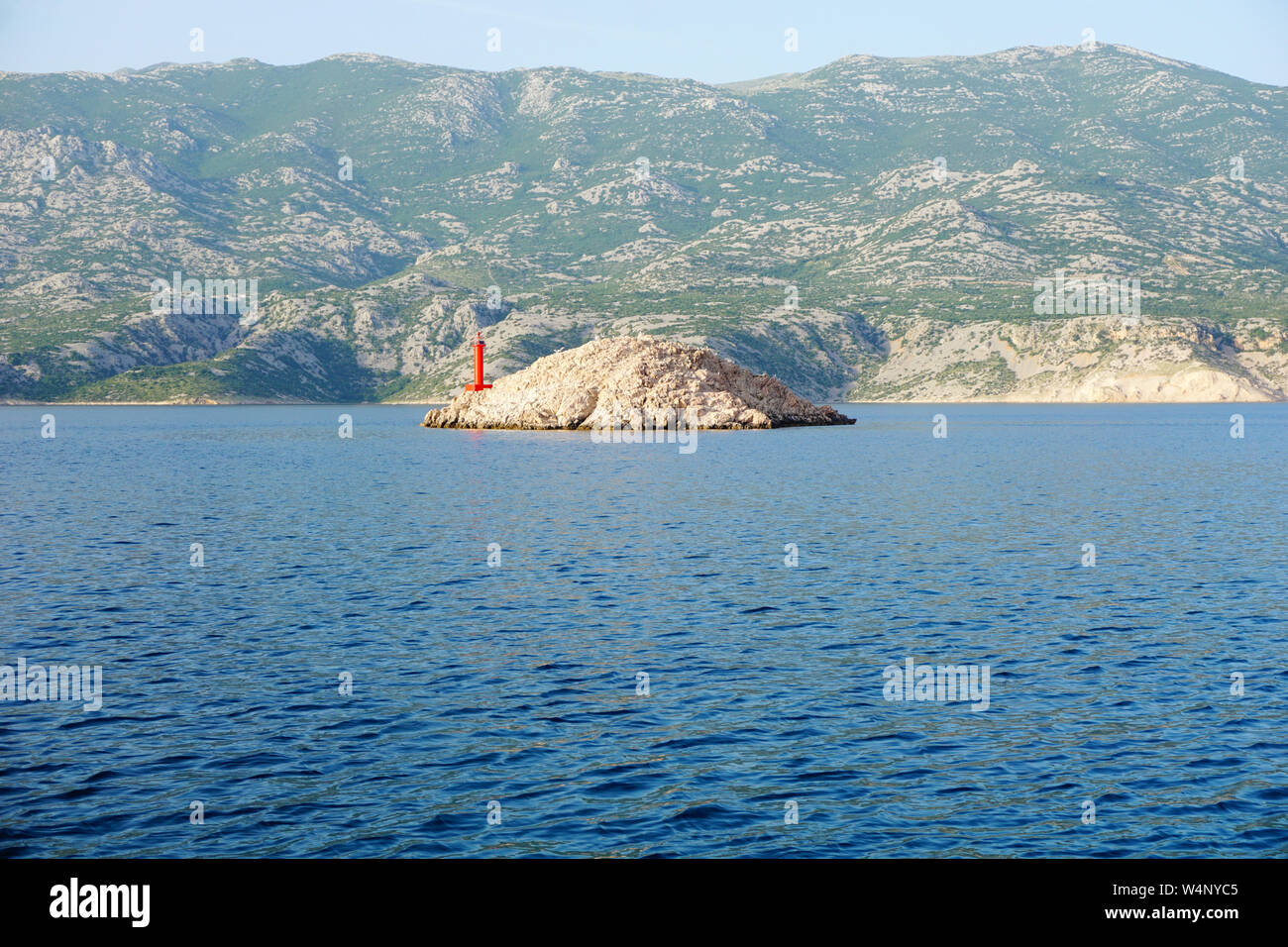 Deep Sea surface bleue en face de la petite île avec le phare rouge et de grandes montagnes en arrière-plan. Belle journée d'été sur le littoral Banque D'Images