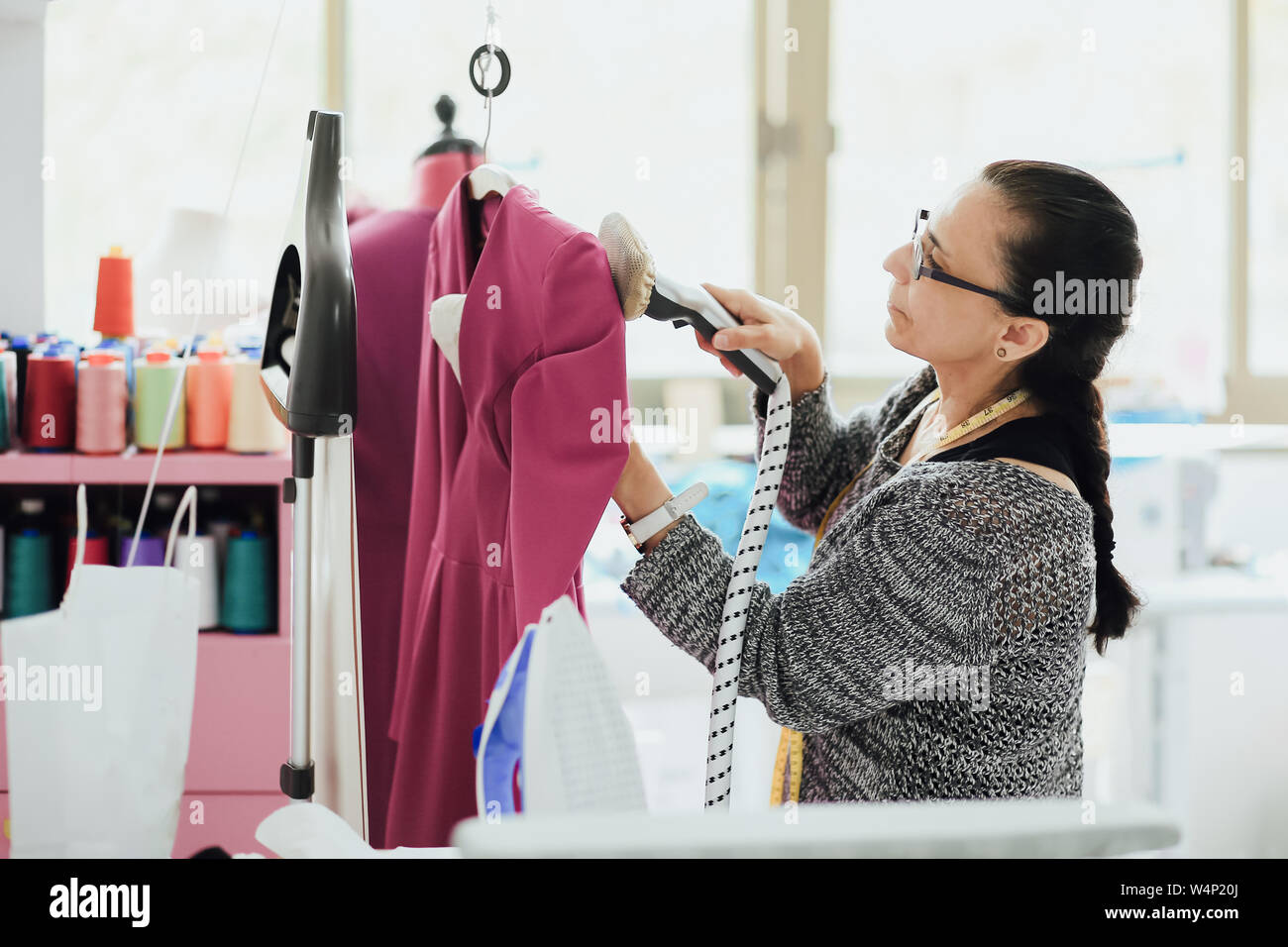 Senior woman with glasses planche une robe dans un studio de design de mode Banque D'Images