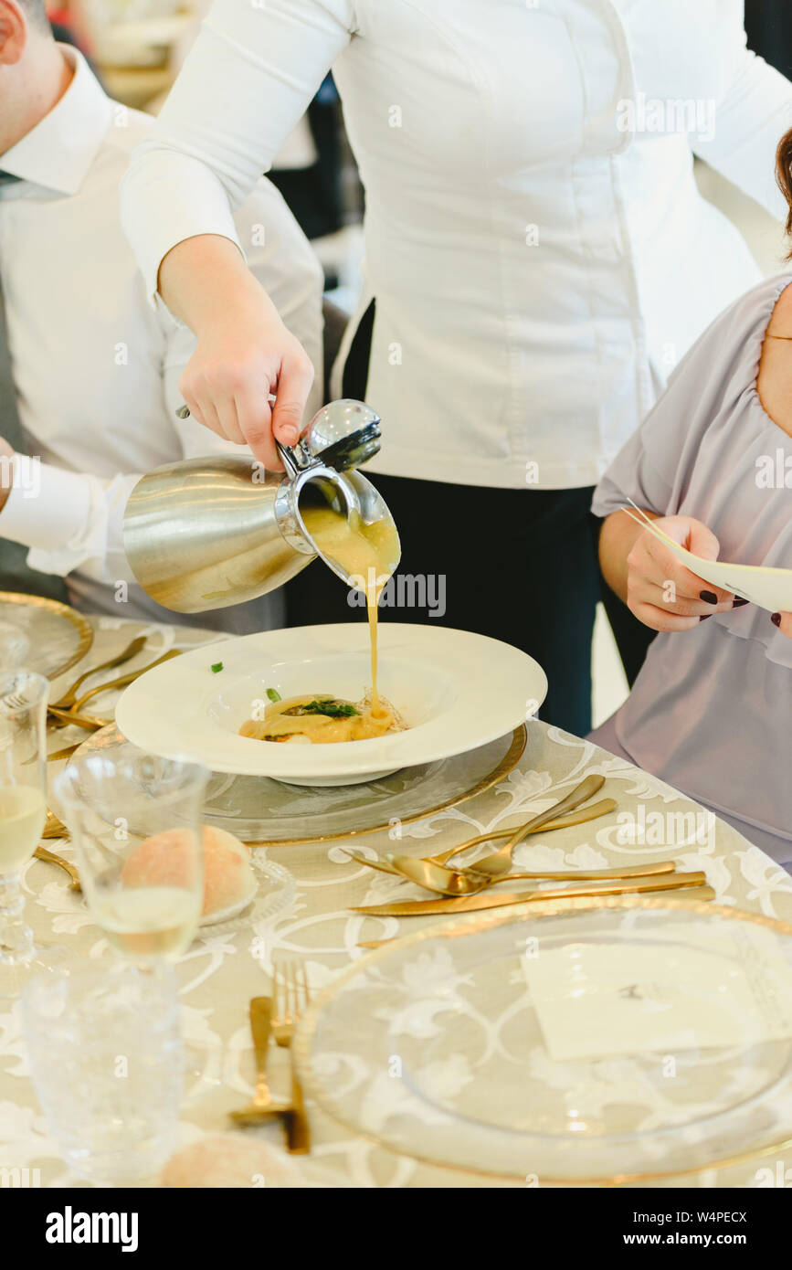 Une sauce se verse dans une assiette de viande dans un restaurant chic. Banque D'Images