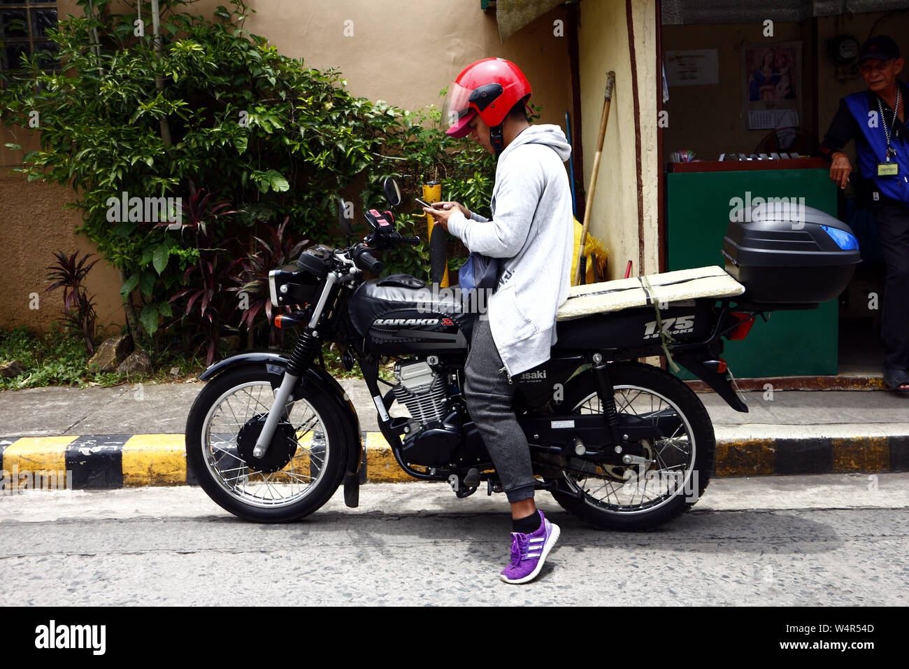 ANTIPOLO CITY, PHILIPPINES - le 23 juillet 2019 : un pilote moto s'arrête à un trottoir de vérifier sur son smartphone. Banque D'Images