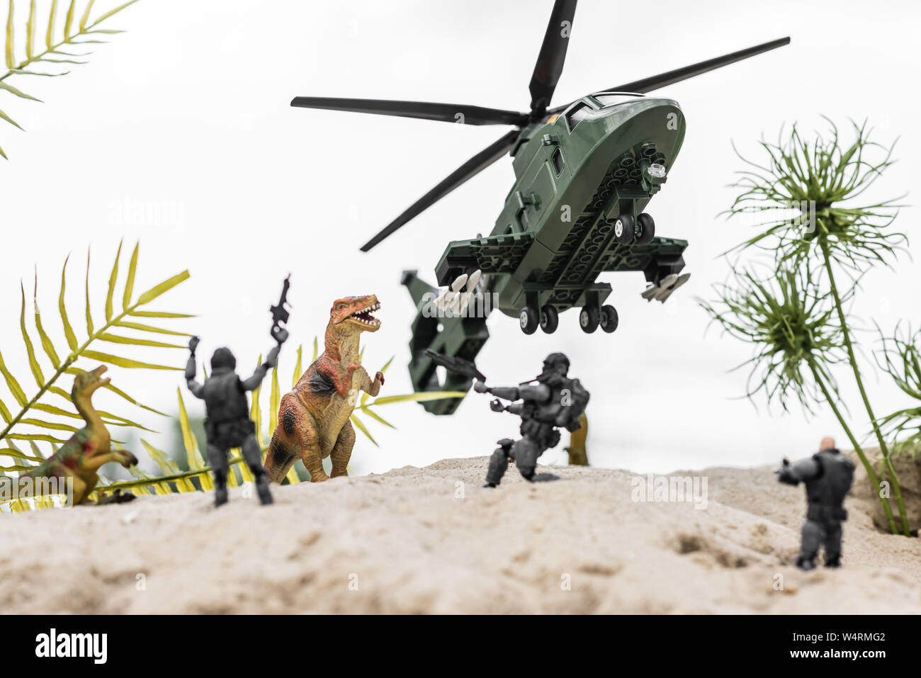 Focus sélectif des soldats en plastique visant à toy dinosaures sur dune de sable avec l'hélicoptère dans le ciel Banque D'Images