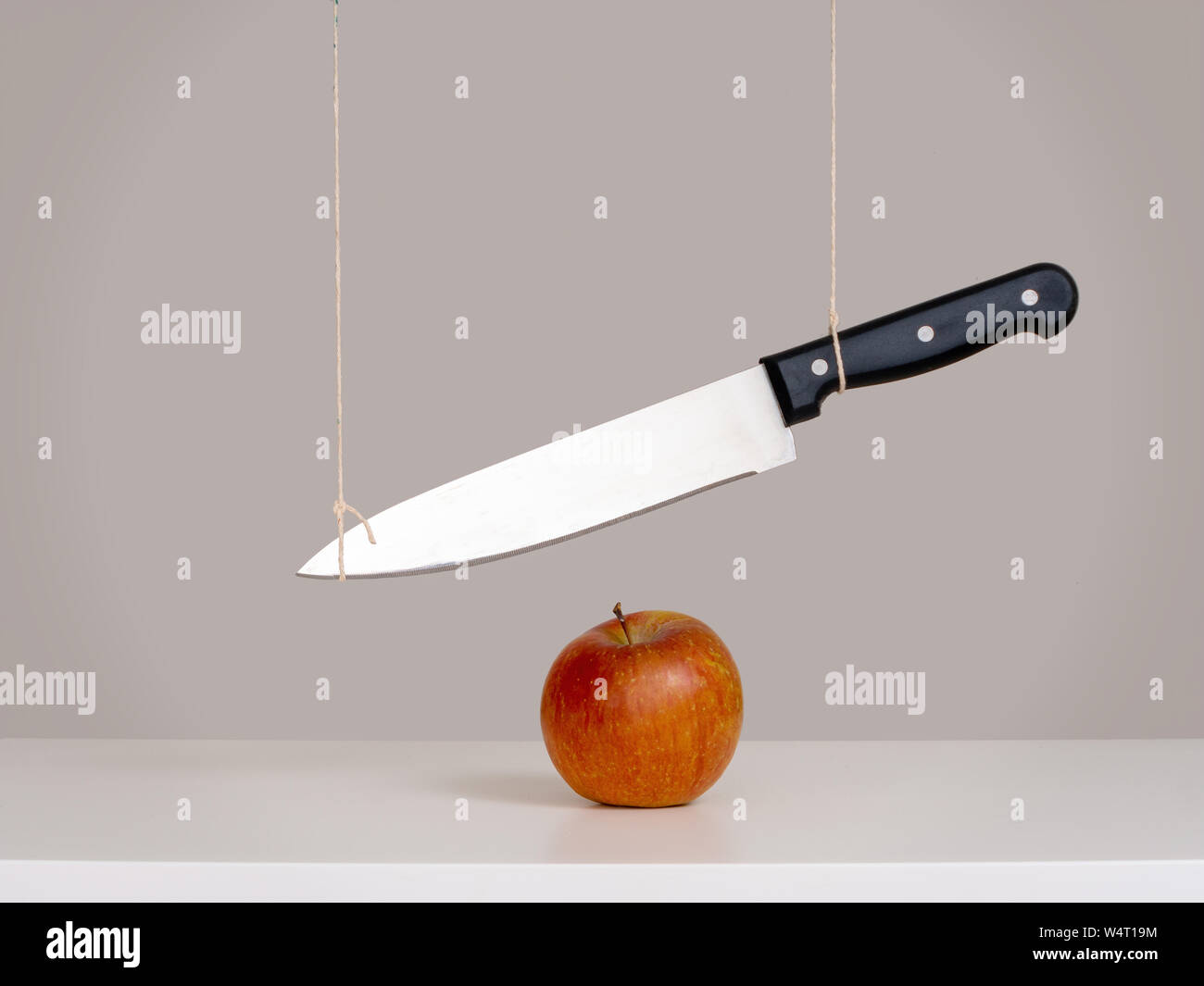 Épée de Damoclès menace, notion de risque, métaphore - grand couteau attaché et suspendu au-dessus d'Apple. La vie encore. Banque D'Images