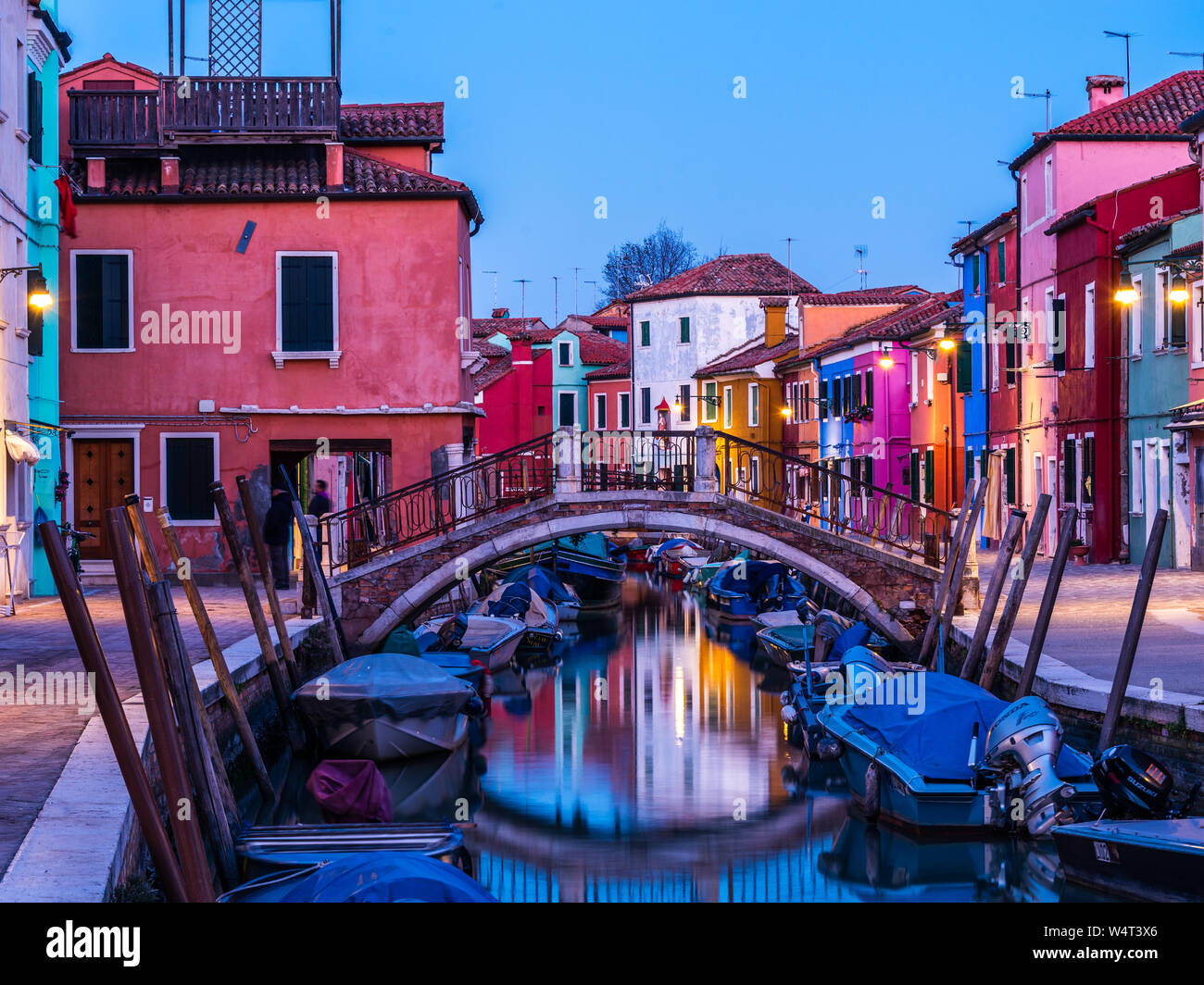 Burano, Italie, 18/11-18. Crépuscule sur la Piazza Baldassare Galuppi aux maisons colorées le long du canal rempli de bateaux couverts. Banque D'Images