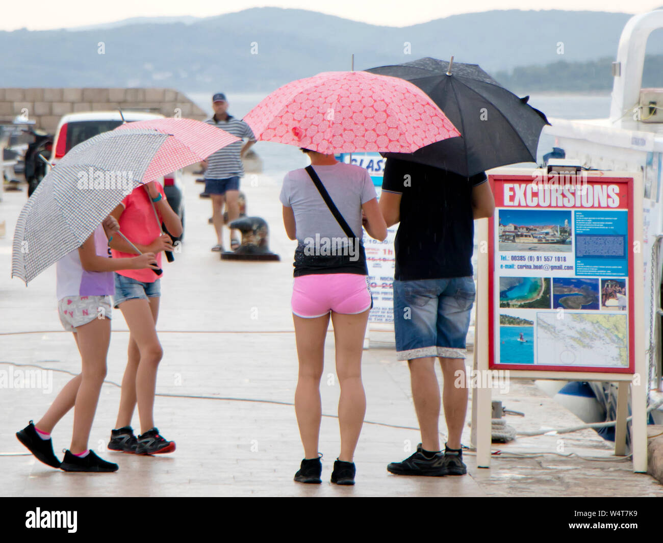 Vodice, Croatie - Juillet 13, 2019 : La famille des parasols en face de panneaux publicitaires de l'excursion en bateau sur un jour d'été pluvieux par la mer Banque D'Images