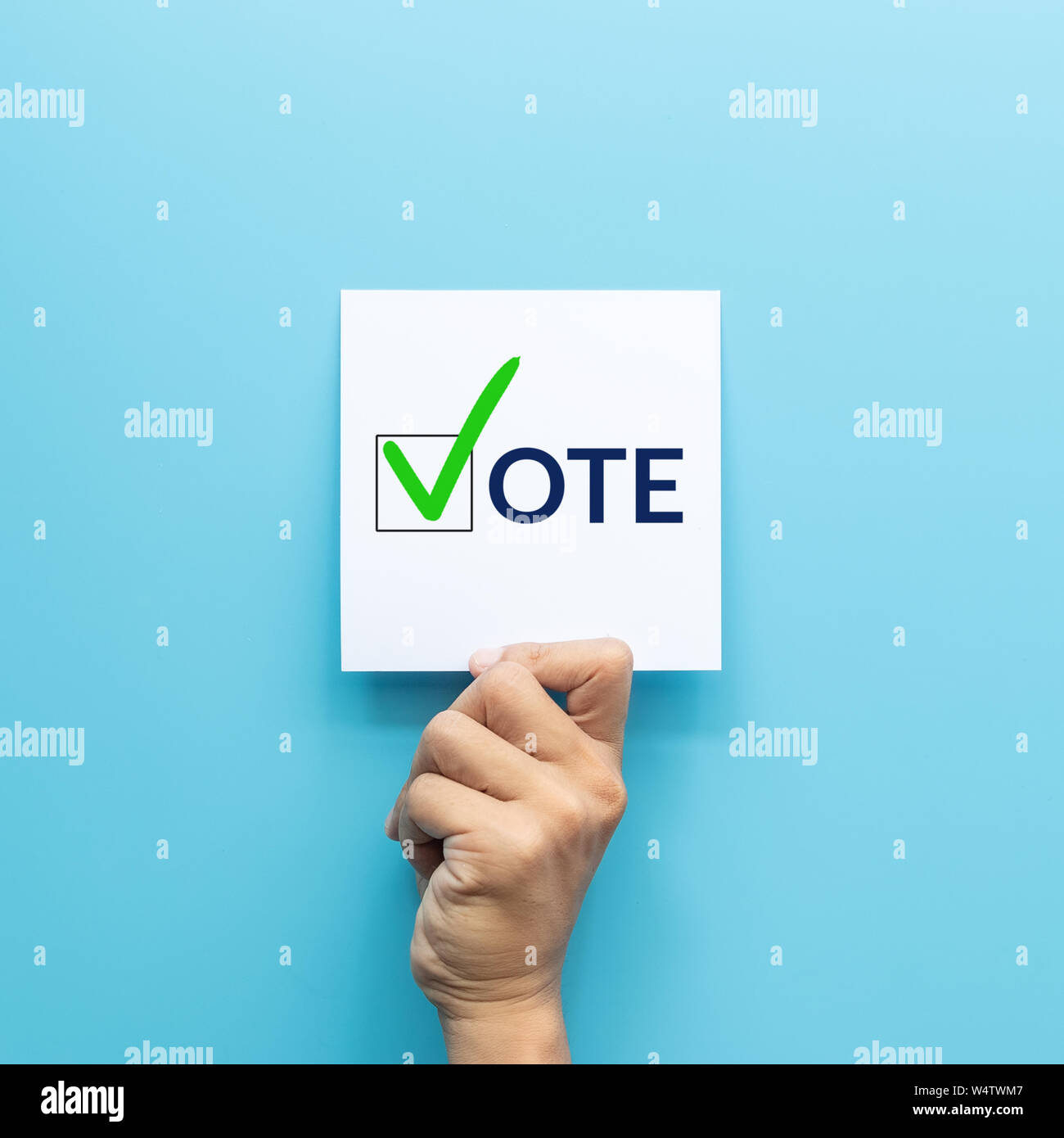 Main tenant du papier blanc avec le "vote" et marque verte symboles vote en case de l'inscription isolé sur fond bleu Banque D'Images