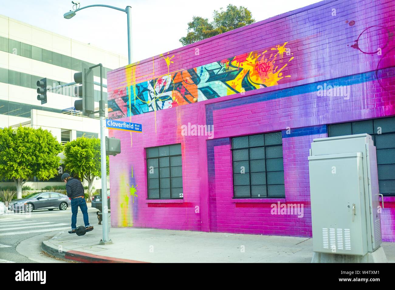 Un jeune homme lecteurs piétons un équilibrage auto électronique au-delà d'un monocycle bâtiment coloré près de Cloverfield Blvd dans la Silicon Beach, le quartier de Los Angeles, Californie, le 10 décembre 2018. () Banque D'Images