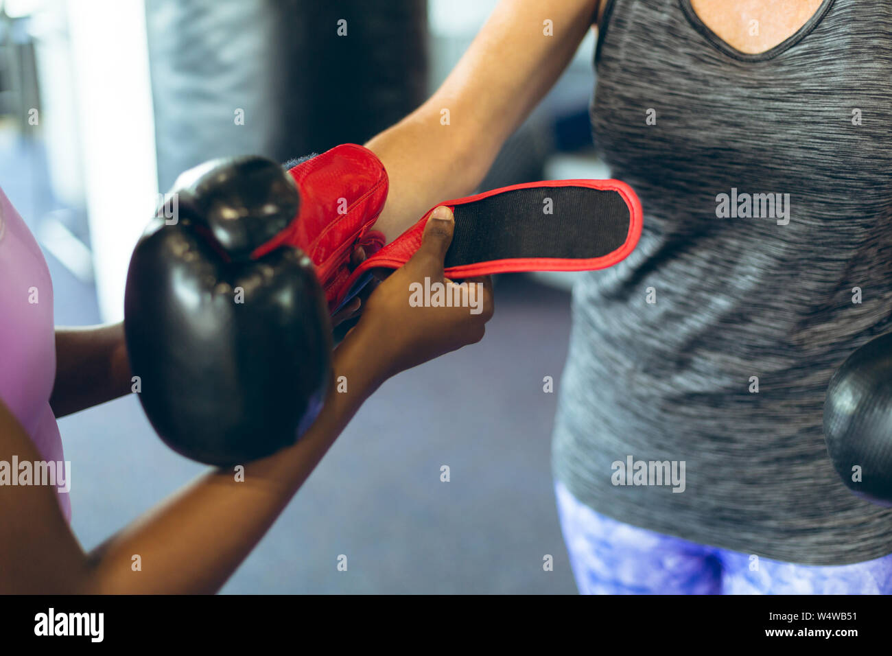 Formateur femelle femelle aidant à porter des gants de boxe athlétique en centre de remise en forme Banque D'Images