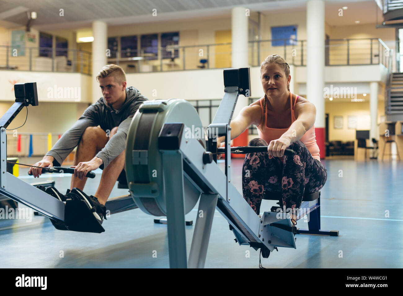Athlète masculin et féminin s'entraîner avec le rowing machine in fitness studio Banque D'Images