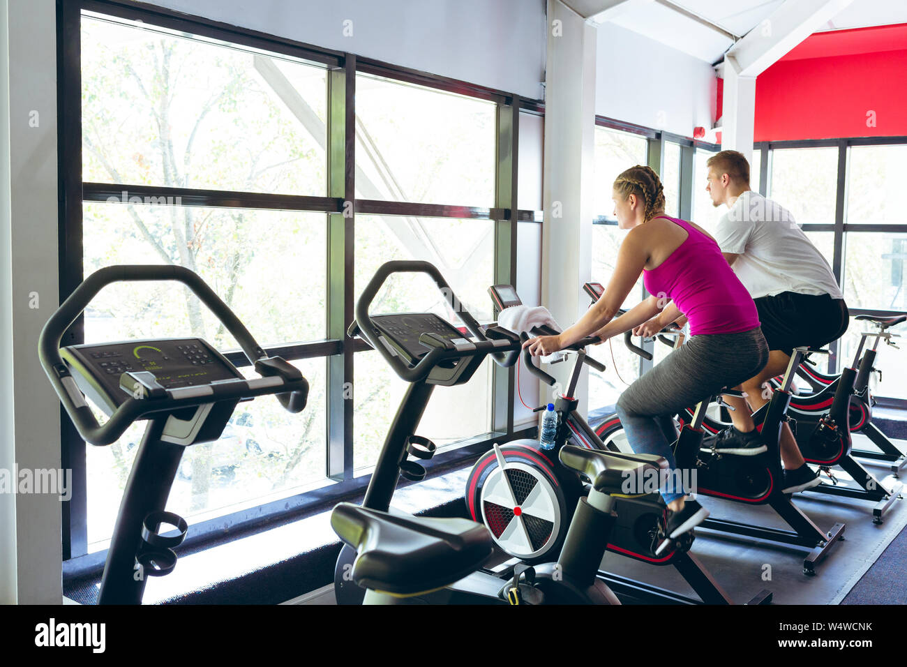 Athlète masculin et féminin s'entraîner avec le vélo d'exercice dans le centre de remise en forme Banque D'Images
