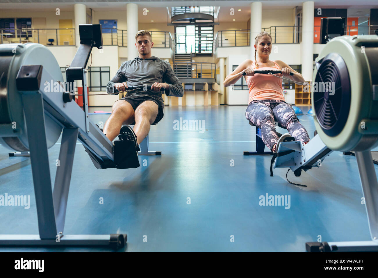 Athlète masculin et féminin s'entraîner avec le rowing machine in fitness studio Banque D'Images