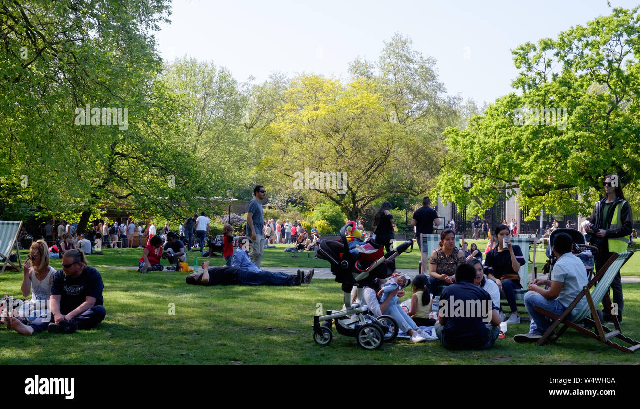 Les Londoniens et les touristes s'asseoir et se coucher sur l'herbe profitant de la journée chaude et ensoleillée à St James's Park, le centre de Londres. Banque D'Images