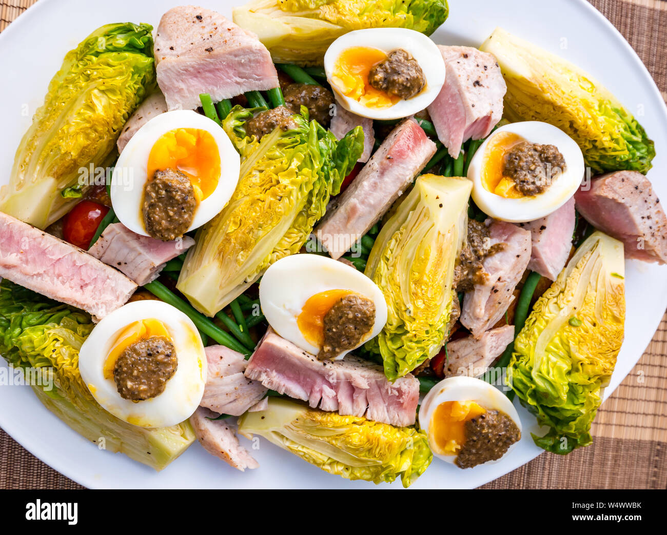 Version de salade niçoise sur plaque blanche. Oeufs durs et d'olive, vinaigrette laitue gem bébé, des pommes de terre et les tranches de steak de thon Banque D'Images