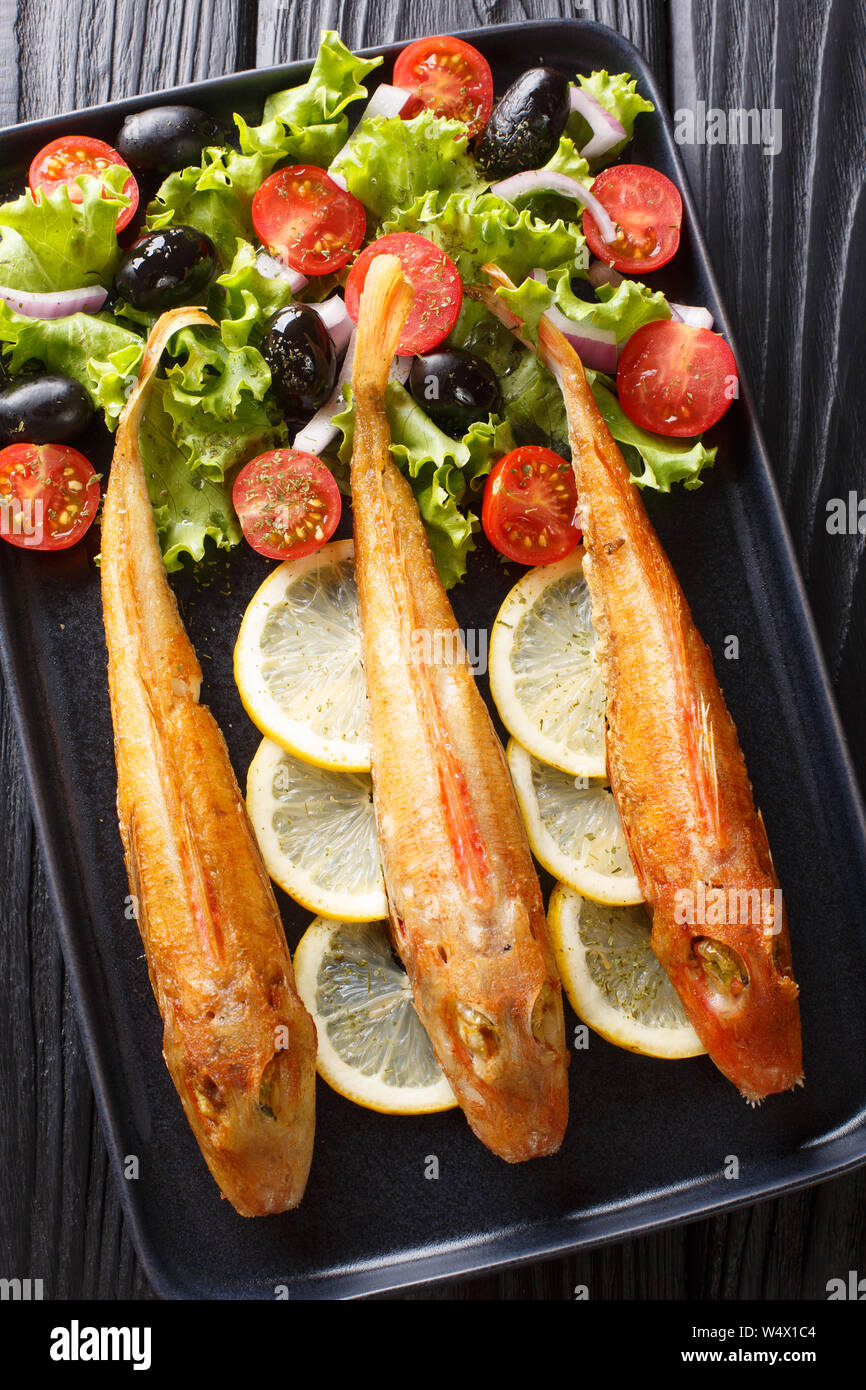 Poisson de mer frits frais et délicieux avec une salade de légumes frais Grondin et citron close-up sur une plaque sur la table. Haut Vertical Vue de dessus Banque D'Images