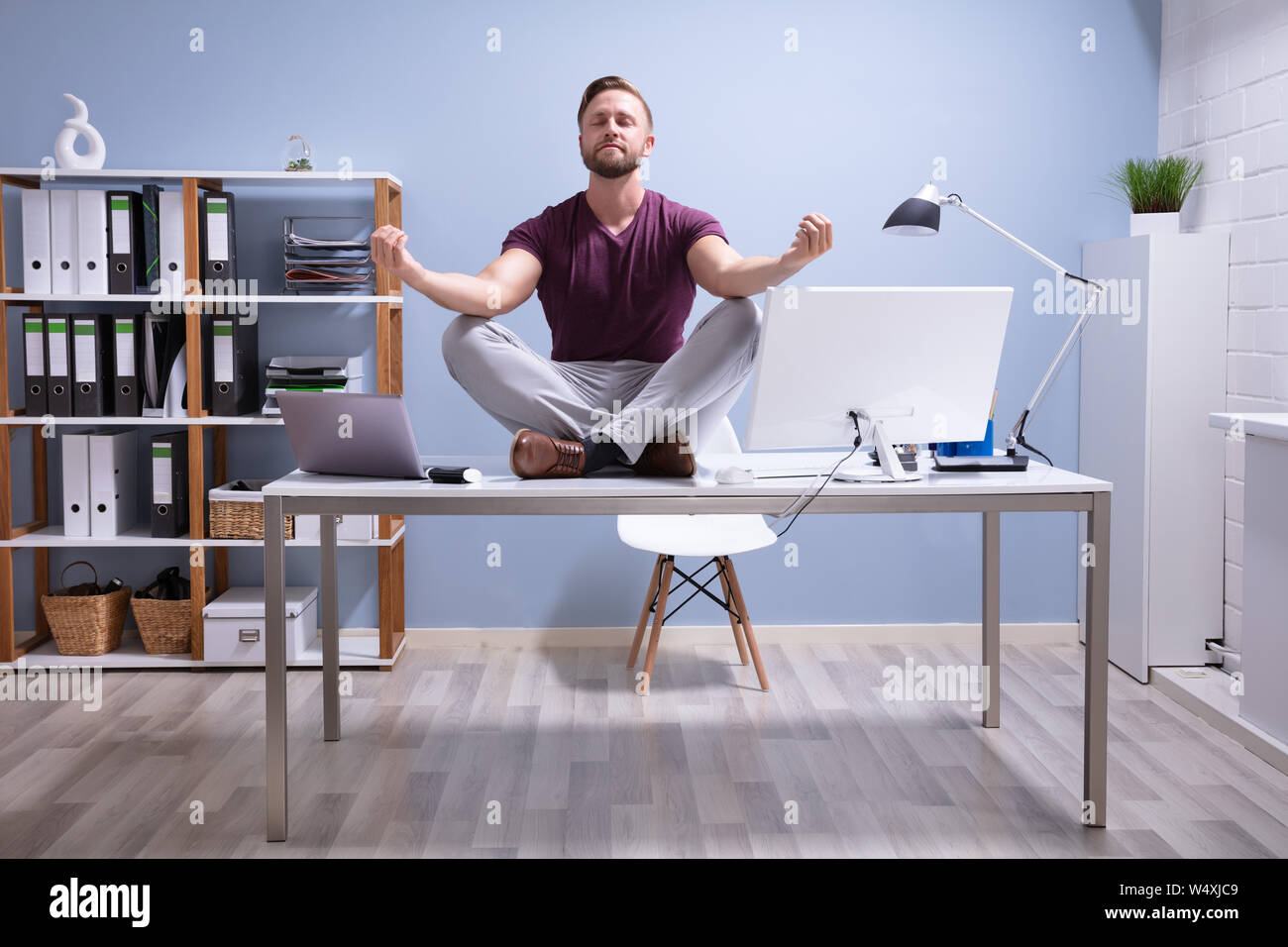 Young Businessman Sitting on Desk In Office Banque D'Images