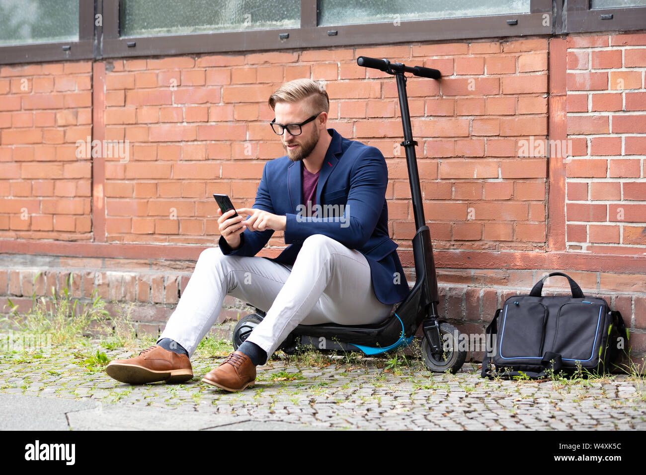 Un beau Businessman Sitting on Scooter électrique à l'aide de téléphone cellulaire près de brick wall Banque D'Images