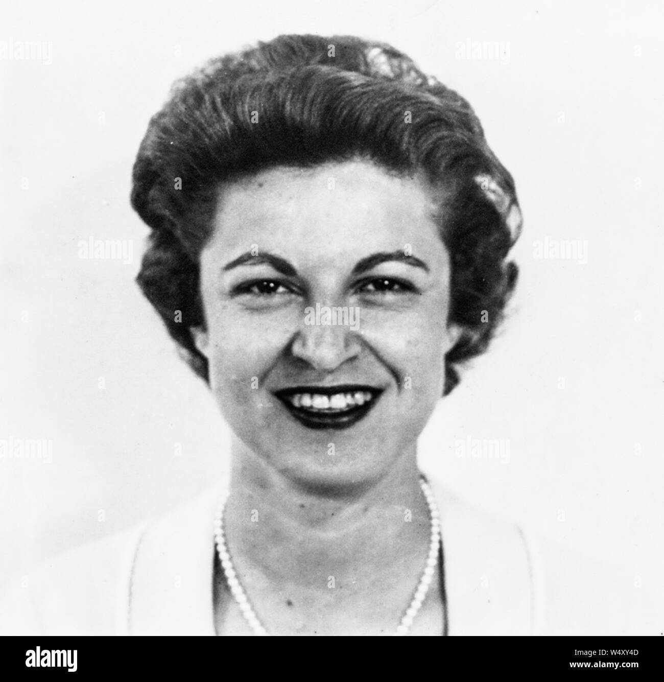 Head and shoulders portrait of a smiling woman wearing rouge à lèvres et un collier de perles, 1960. () Banque D'Images