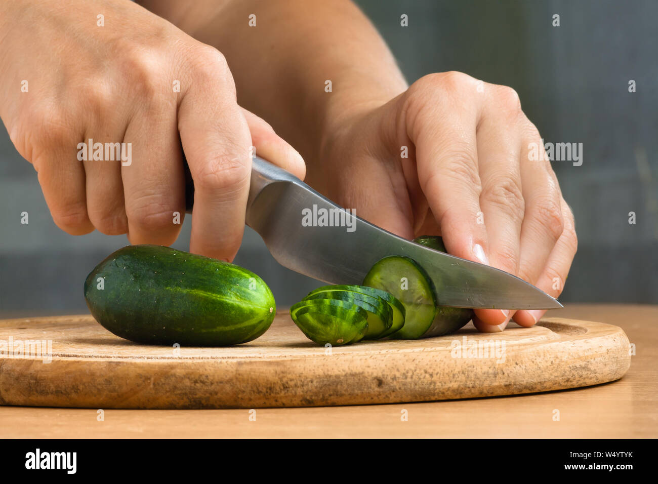 Mains de woman slicing sur le concombre planche à découper en bois Banque D'Images