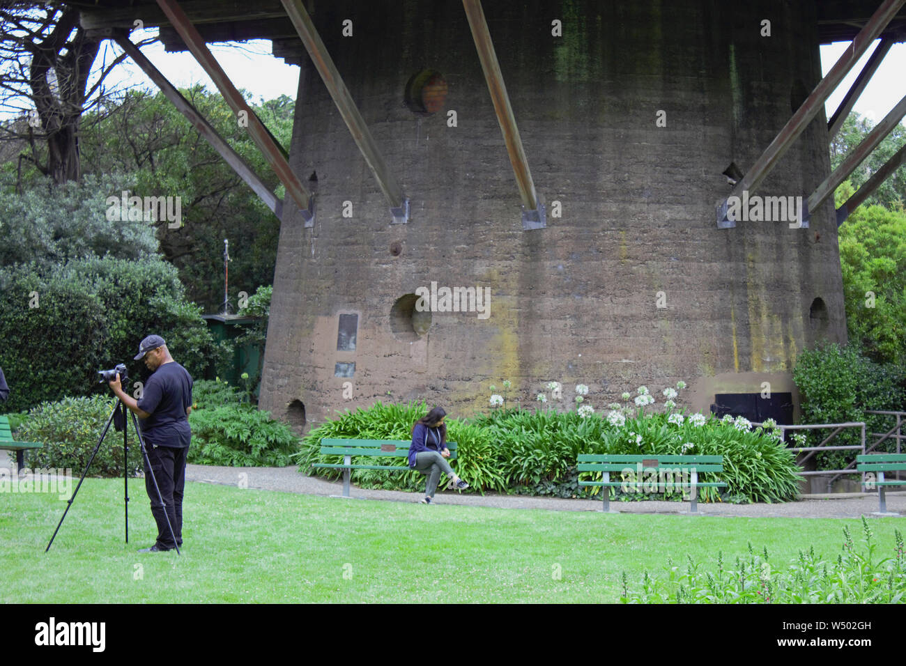 Un photographe se concentre sur son sujet que le dirigeant d'une femme assise sur un banc sous l'un des nombreux moulins à vent dans la région de San Francisco's Golden Gate Park. Banque D'Images