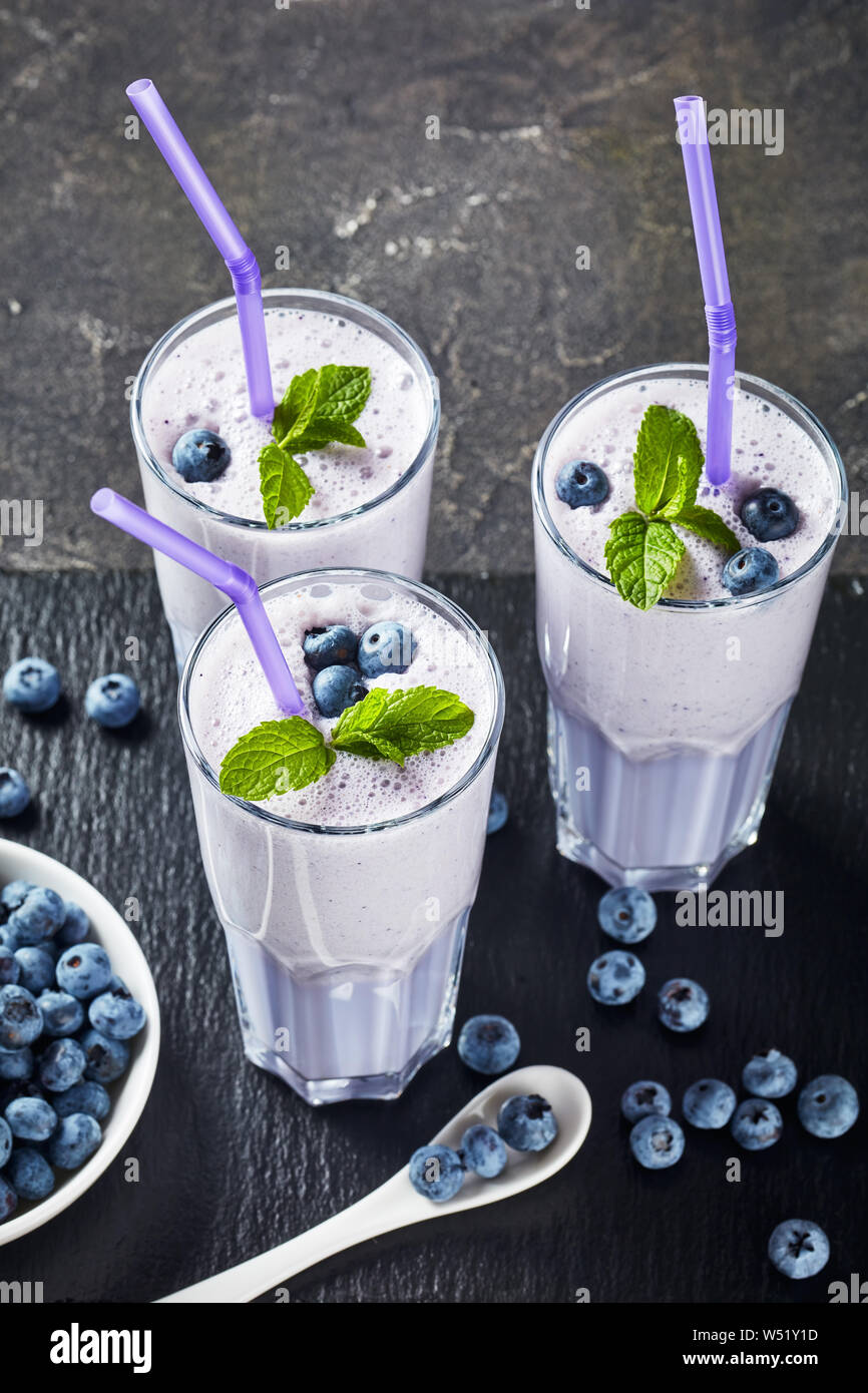 Smoothie aux bleuets mousse de lait de coco dans trois verres avec paille sur un plateau en ardoise noire sur une table en béton, vertical Vue de dessus Banque D'Images