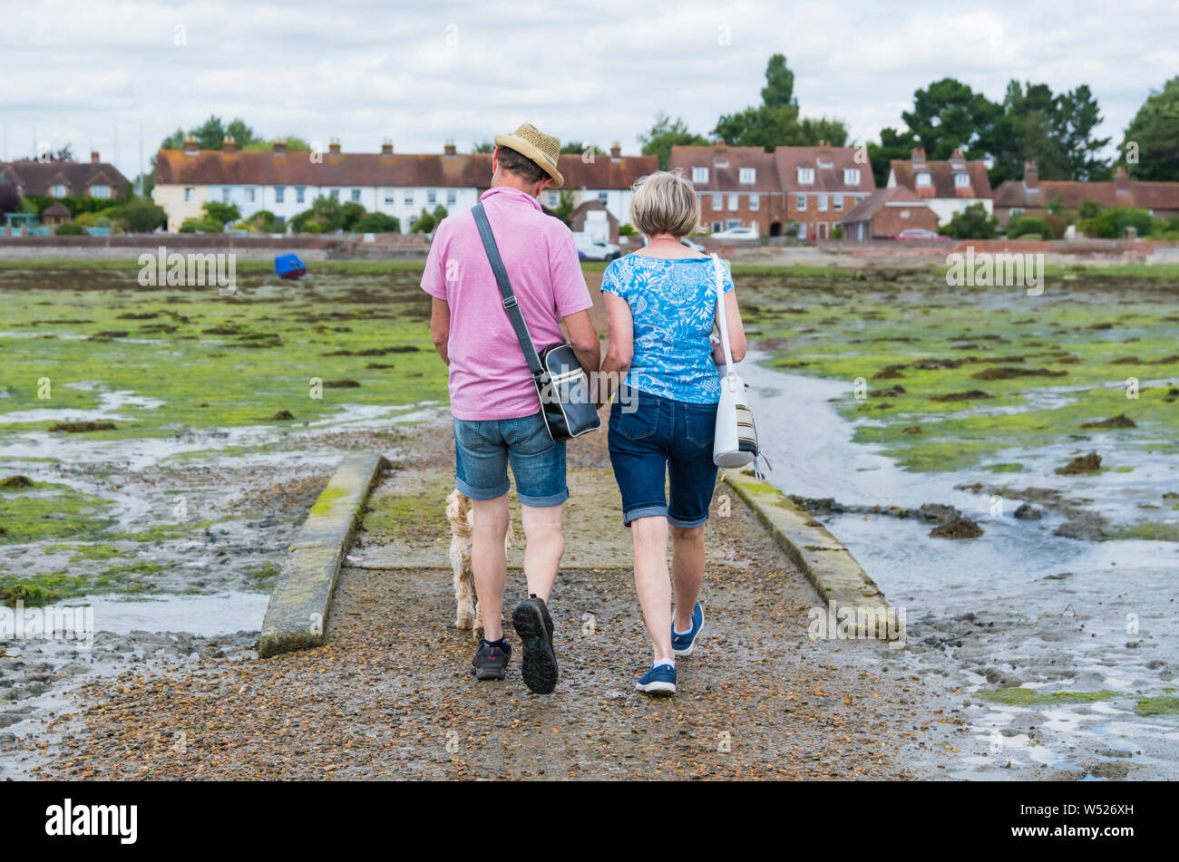 Un couple holding hands walking across Bosham Causeway à marée basse dans le port de Chichester, Bosham Village, West Sussex, Angleterre, Royaume-Uni. Banque D'Images