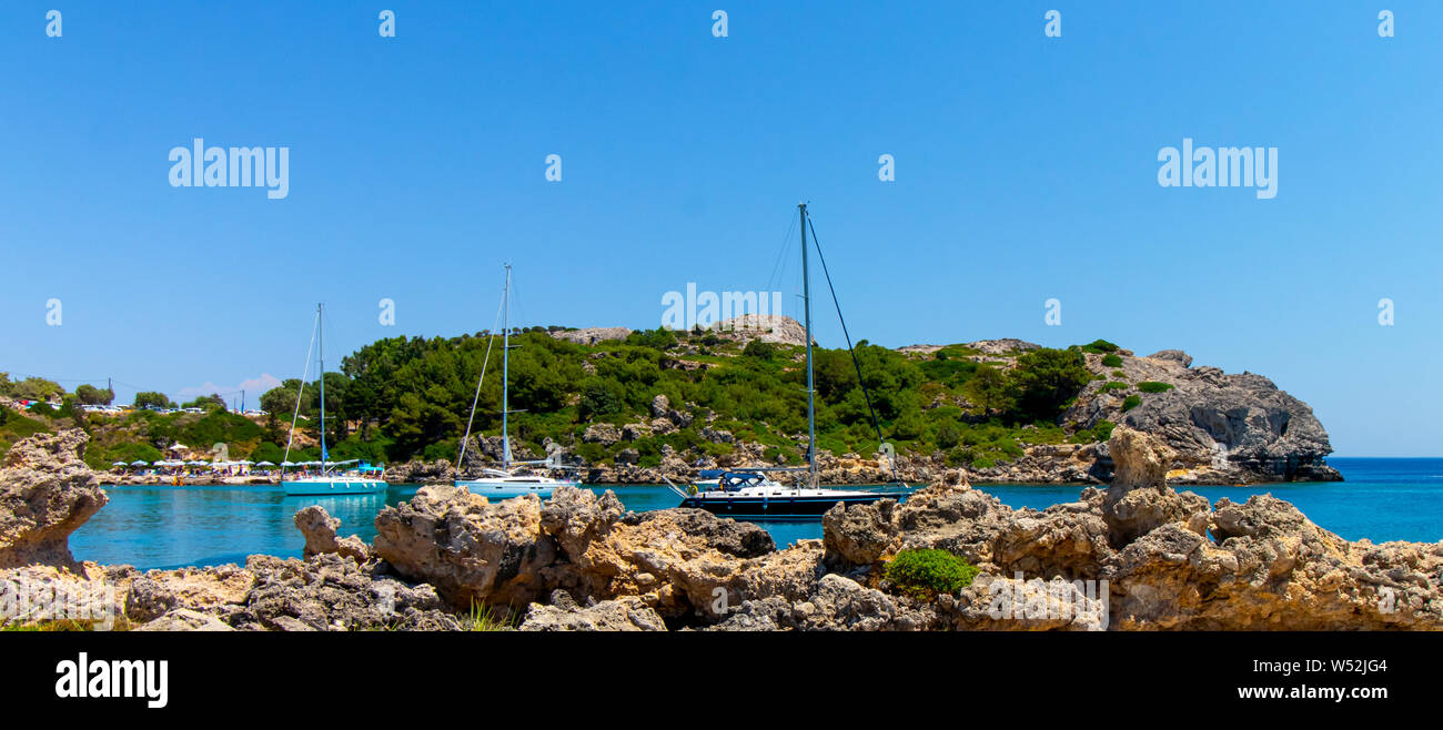 Une baie sur l'île de Rhodes avec les bateaux à voile et des rochers en premier plan Banque D'Images