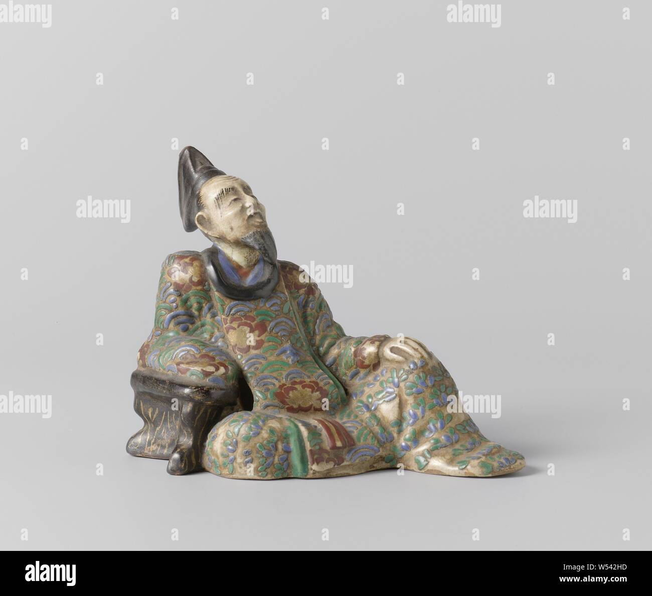 La figure de la polit inclinables Kinomoto no Hitomaro, statue en porcelaine, peintes sur l'émail en bleu, rouge, vert, noir et or. L'image représente le poète assis Kinomoto pas de Hitomaro, appuyée sur une souche d'arbre. Décoration de l'émail. style Ninsei, anonyme, le Japon, l'c. 1750 - c. 1868, période Edo (1600-1868), Porcelaine, glaçure (matériel), de l'or (métal), la vitrification, h 10,7 cm × 14,2 cm × w d 7,7 cm Banque D'Images