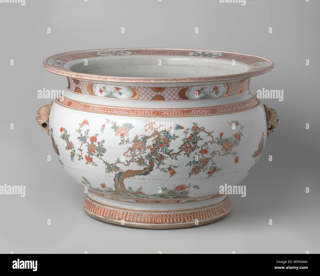 Fish Bowl avec des plantes à fleurs, les animaux et les têtes de lion en porcelaine moulée, bocal à poissons avec un corps sphérique, bord plat et la diffusion de la base, peint sur la glaçure en bleu, rouge, vert, jaune, aubergine, noir et or. Sur le mur extérieur deux fois l'arbre avec des plantes à fleurs. Entre les deux, un modèle général d'un shishi (chien lion) deux fois avec les supports de bague d'un chrysanthème fleurs ci-dessous. Sur l'épaule un groupe avec nappes travail interrompu en alternant ensemble et la moitié des fleurs de lotus. La face inférieure du mur avec une bande de chrysanthèmes sur frogsilk interrompue par des cartouches avec des plantes. Le cou Banque D'Images