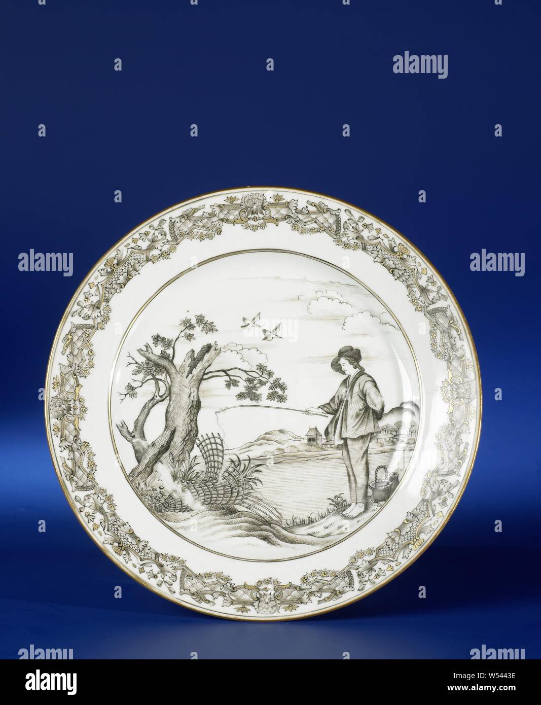 La plaque avec une image du jeune pêcheur, assiette de porcelaine, peint sur la glaçure en noir et or. Sur la télévision un jeune homme avec une canne à pêche sur le bord d'une rivière, derrière lui un panier, jug et le poisson et en face de lui un arbre mort et deux pièges, de l'autre côté de la rivière un village avec des montagnes, la frontière avec un motif décoratif. Sur le bas de deux anciennes étiquettes avec 'F. Bodenham / Elmhurst, Hereford / '52 et '16 / Le pêcheur / [...]". Présentation basée sur l'impression De Jonge Visser par Abraham Bloemaert (1564-1651). Salon européen en encre de Chine., anonyme, de la Chine, c Banque D'Images