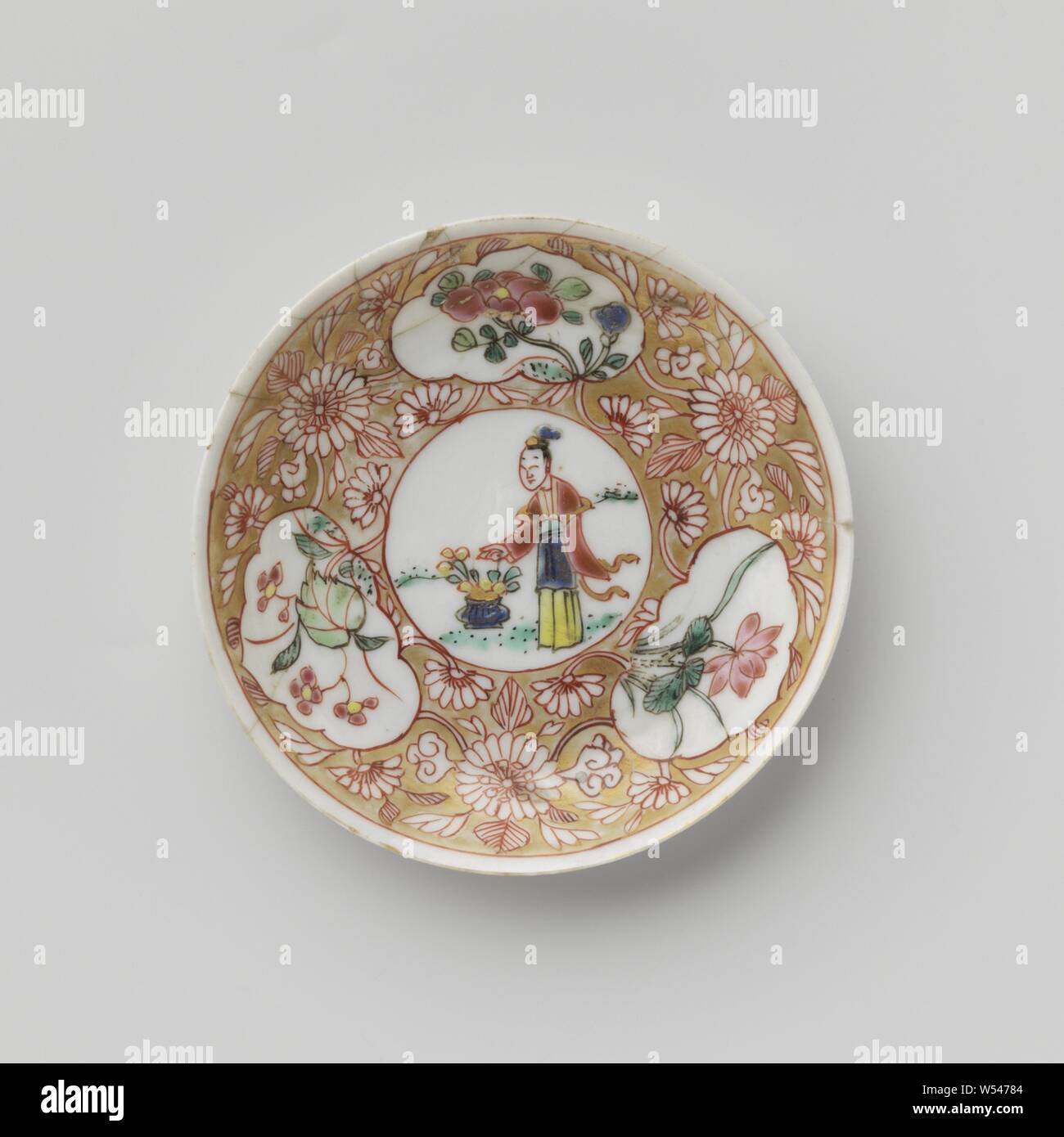 Soucoupe d'une dame avec panier de fleurs et de plantes à fleurs dans les panneaux, plat en porcelaine avec diffusion, mur peint sur l'émail en bleu, rouge, rose, vert, noir et or. Sur la plaque du plat un médaillon avec une dame dans un paysage avec un panier de fleurs, de fleurs de vignes qui ont été enregistrés dans le médaillon et trois cartouches avec des plantes à fleurs (y compris lotus) dans la masse d'or. Plat a été brisée. Famille rose., anonyme, la Chine, l'c. 1725 - c. 1749, dynastie Qing-(1644-1912) / Yongzheng-période (1723-1735) / période de Qianlong (1736-1795), Porcelaine, glaçure (matériel), de l'or (métal Banque D'Images