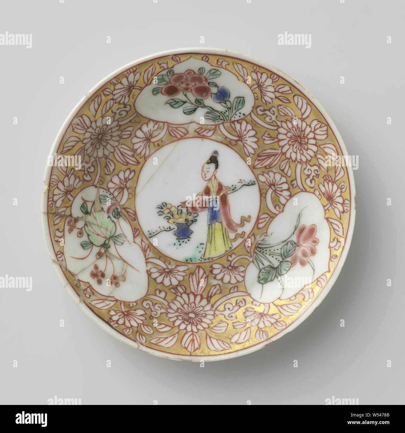 Soucoupe d'une dame avec panier de fleurs et de plantes à fleurs dans les panneaux, plat en porcelaine avec mur peint sur l'épandage en émail bleu, rouge, rose, vert, noir et or. Sur la plaque du plat un médaillon avec une dame dans un paysage avec un panier de fleurs, de fleurs de vignes qui ont été enregistrés dans le médaillon et trois cartouches avec des plantes à fleurs (y compris lotus) dans la masse d'or. Plat a été brisée. Famille rose., anonyme, la Chine, l'c. 1725 - c. 1749, dynastie Qing-(1644-1912) / Yongzheng-période (1723-1735) / période de Qianlong (1736-1795), Porcelaine, glaçure (matériel), de l'or (métal Banque D'Images