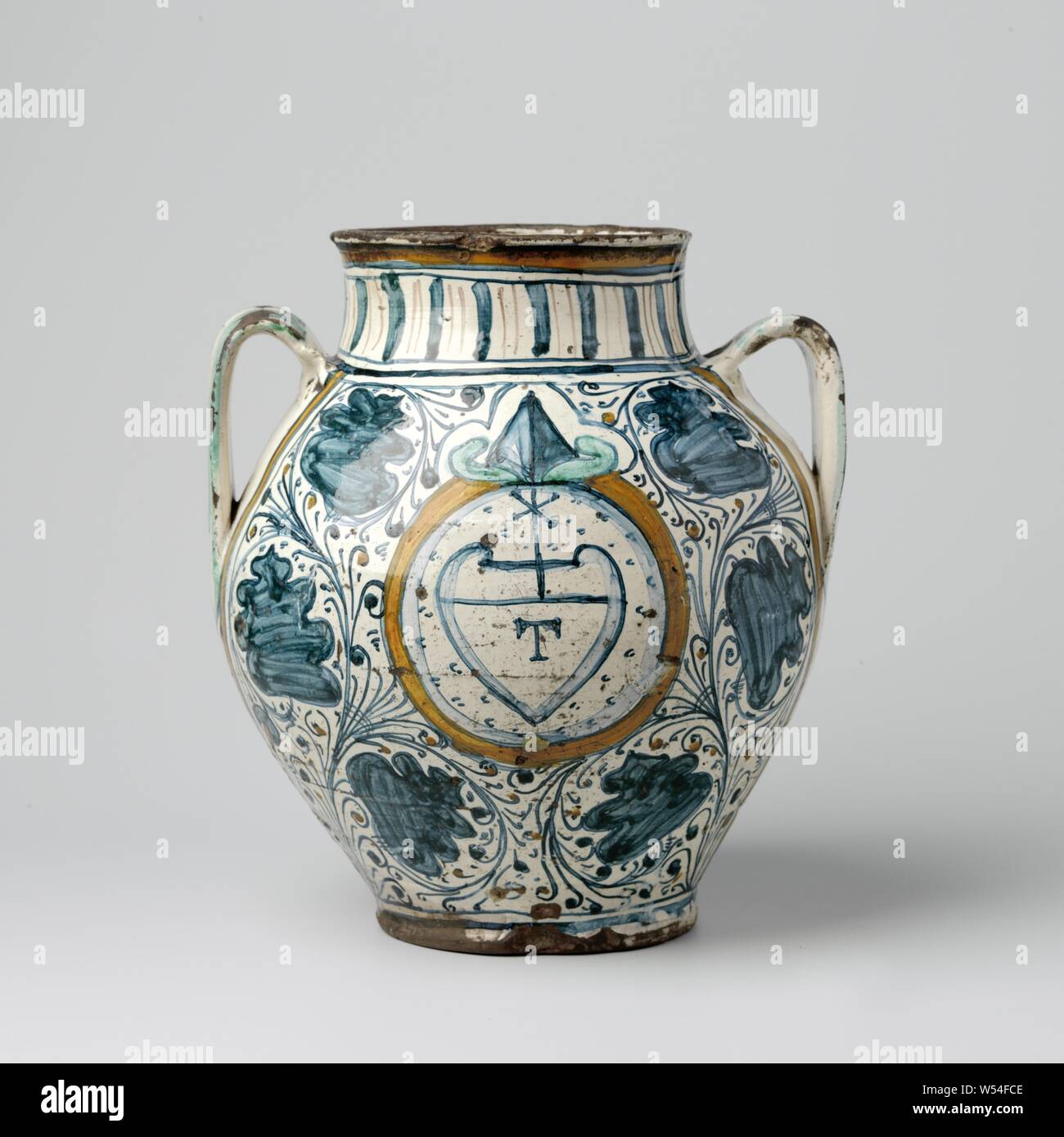 Vase, sphérique, avec deux oreilles, vase sphérique de majolique peint multicolores, avec un court col cylindrique en forme de c et deux oreilles. À l'avant de la vase un arme en forme de coeur est peint dans un médaillon circulaire, l'intérieur de laquelle la lettre T et au-dessus de laquelle une croix. Autour du médaillon et à l'arrière du vase, les vignes sont peints avec des spirales, entre lesquels sont de grandes fleurs stylisées bleu., anonyme, Montelupo, c. 1460 - c. 1490, faïence, émail étain, plomb glaze, h 30,0 cm d 15,5 cm d 27 cm Banque D'Images
