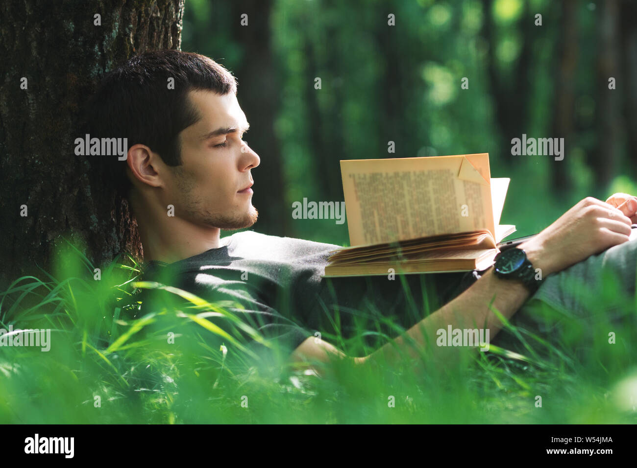 Cute young Caucasian man dans le parc de dormir sur l'herbe avec un livre. Lire un livre dans le parc dans le matin d'été Banque D'Images