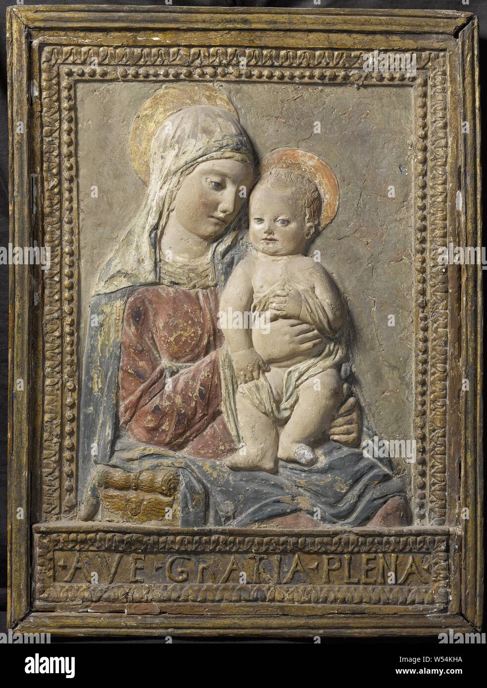 Vierge à l'enfant, mi-Vierge à l'enfant, en relief, de stuc polychrome et doré. Assis, illustré aux genoux et de trois-quarts vers la droite. Maria porte un voile sur la tête. L'enfant, de face, est placé sur ses genoux dans la moitié debout, moitié assis. Elle prend en charge la jambe gauche avec les doigts d'une main, avec l'autre main, elle appuie sur l'enfant qui détient une partie de ses attaches dans chaque main contre elle. Une partie de l'arrière de la chaise pliante se compose d'une volute en vertu de laquelle un chérubin est visible. Châssis profilé avec bords de feuille et perle et un socle sur lequel AVE GRATIA PLENA Banque D'Images