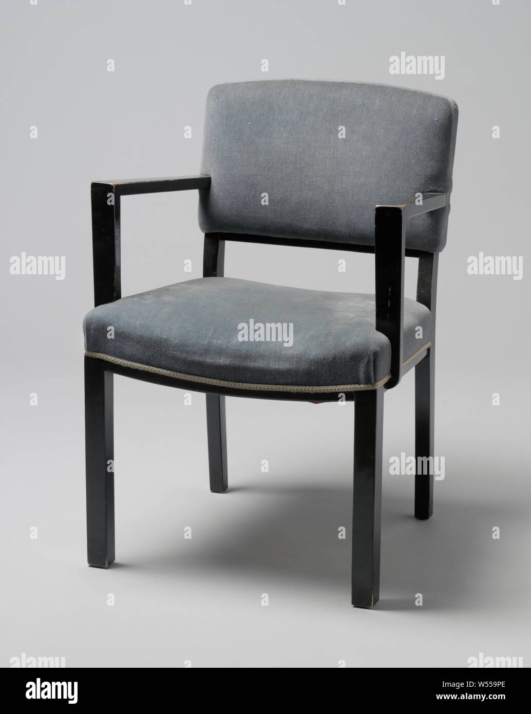 Fauteuil avec accoudoirs anguleux et couverte de bande bleue, Fauteuil de bois laqué noir reposant sur quatre pieds carrés. Les pattes avant sont droites et les pattes postérieures sont légèrement pliés et continuer à l'arrière. Le siège est réglé en quatre lignes, les deux lignes de côté qui sont droits et les lignes avant et arrière plié. Le bas de caisse le dossier est aussi tordue. Télévision accoudoirs angulaire délabré du centre du dossier et reste à l'avant, pas en ligne avec les pattes avant, sur la télévision, qui sont partiellement struts attaché à et en partie contre le siège. La main courante et le siège sont Banque D'Images