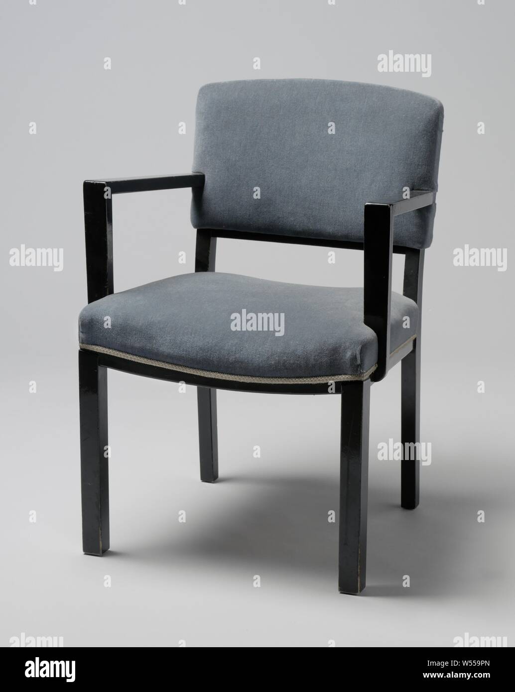 Fauteuil avec accoudoirs anguleux et couverte de bande bleue, Fauteuil de bois laqué noir reposant sur quatre pieds carrés. Les pattes avant sont droites et les pattes postérieures sont légèrement pliés et continuer à l'arrière. Le siège est réglé en quatre lignes, les deux lignes de côté qui sont droits et les lignes avant et arrière plié. Le bas de caisse le dossier est aussi tordue. Télévision accoudoirs angulaire délabré du centre du dossier et reste à l'avant, pas en ligne avec les pattes avant, sur la télévision, qui sont partiellement struts attaché à et en partie contre le siège. La main courante et le siège sont Banque D'Images